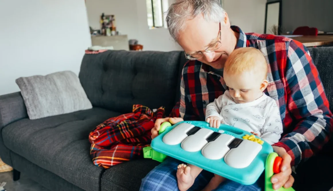 Abuelo feliz jugando con su nieta bebé que toca un piano de juguete