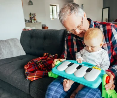 Abuelo feliz jugando con su nieta bebé que toca un piano de juguete