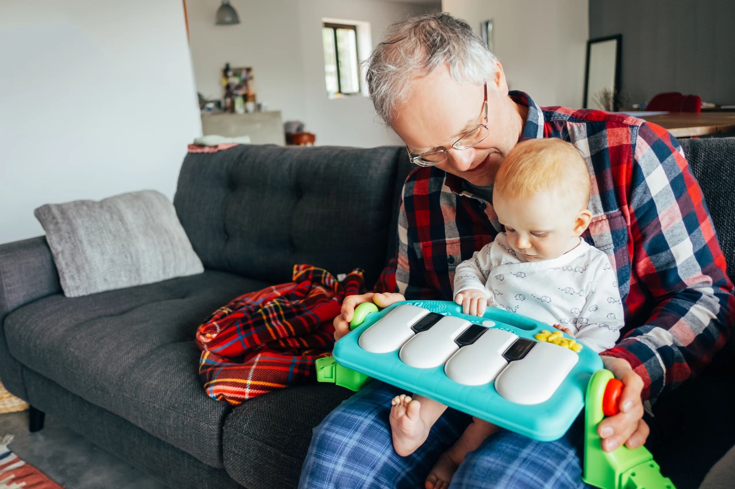Abuelo feliz jugando con su nieta bebé que toca un piano de juguete Abuelo feliz jugando con su nieta bebé que toca un piano de juguete